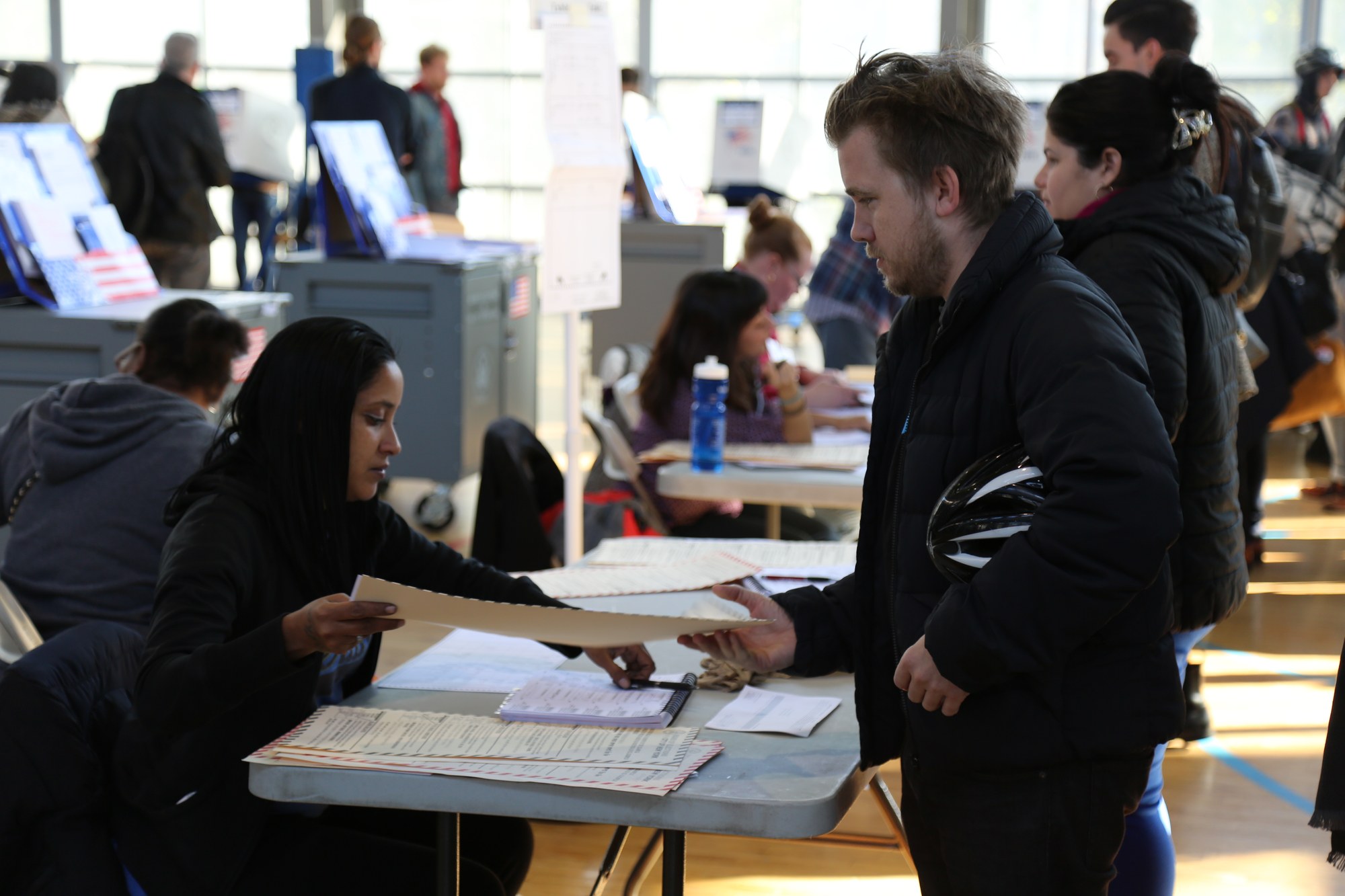 Poll worker hands a paper ballot to a voter at a U.S. polling station with voting booths in the background
