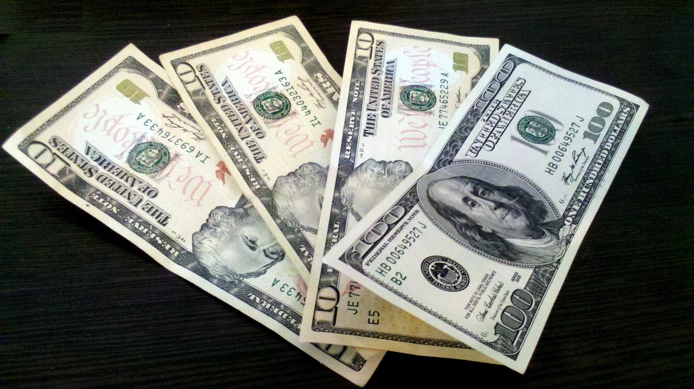 U.S. Federal Reserve notes — $100 and $10 bills fanned on a dark surface