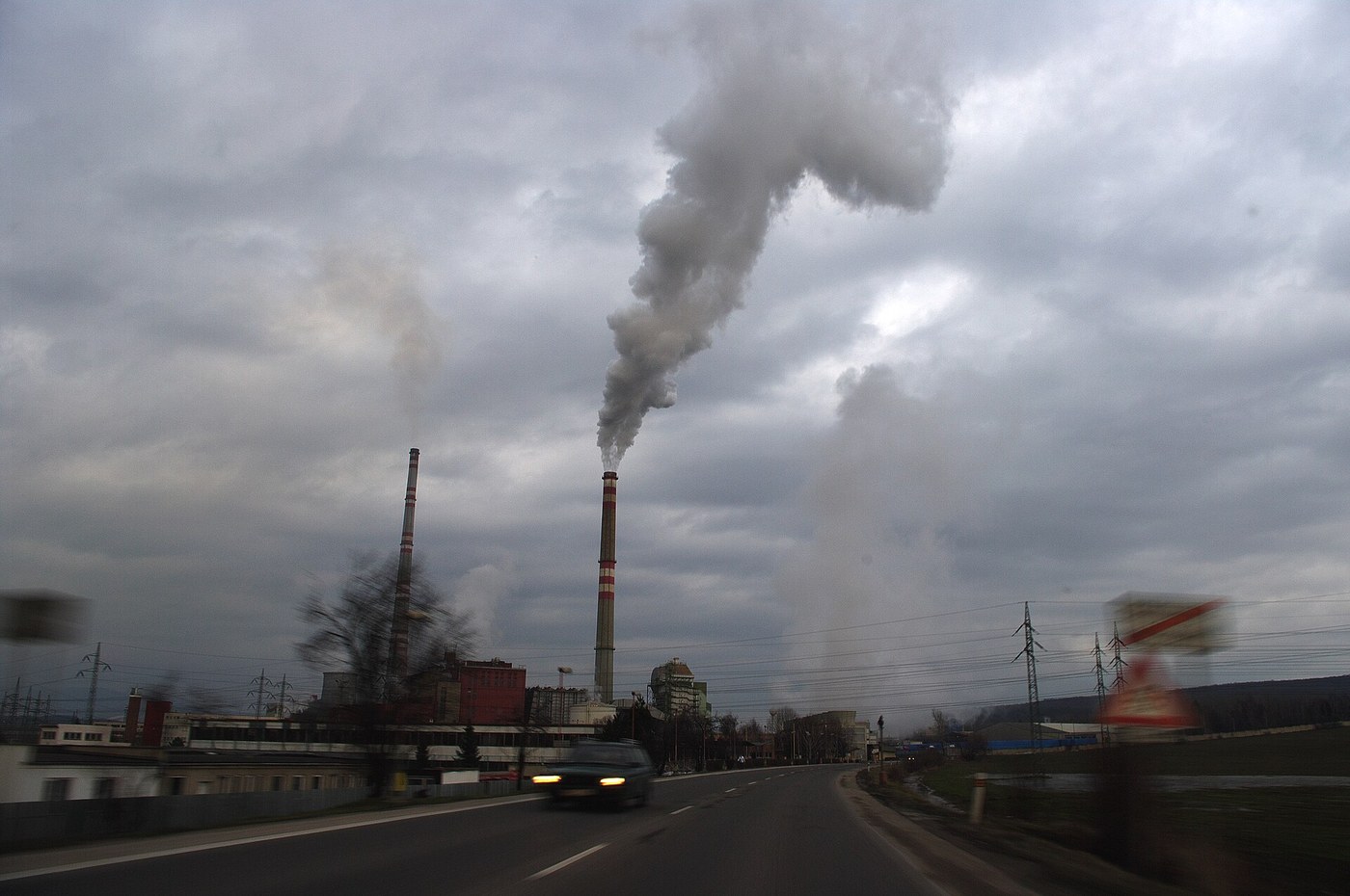 Industrial power-plant smokestacks emitting plumes beside a road