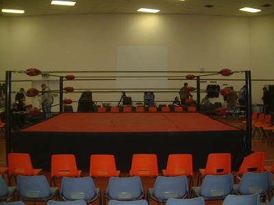 Professional wrestling ring with folding chairs in a small indoor hall