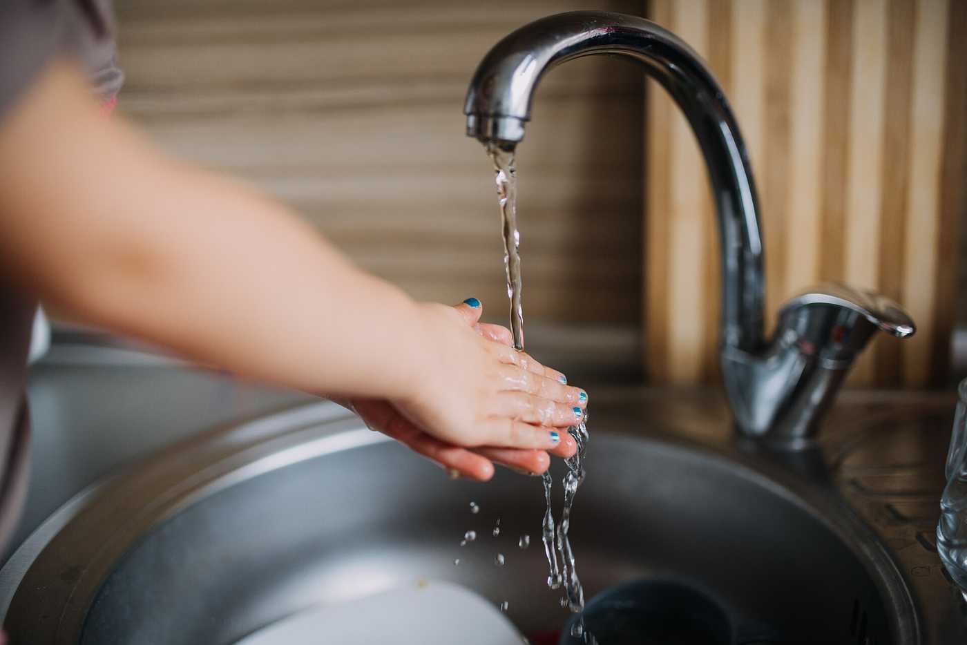 Child washing hands under running water at a kitchen sink