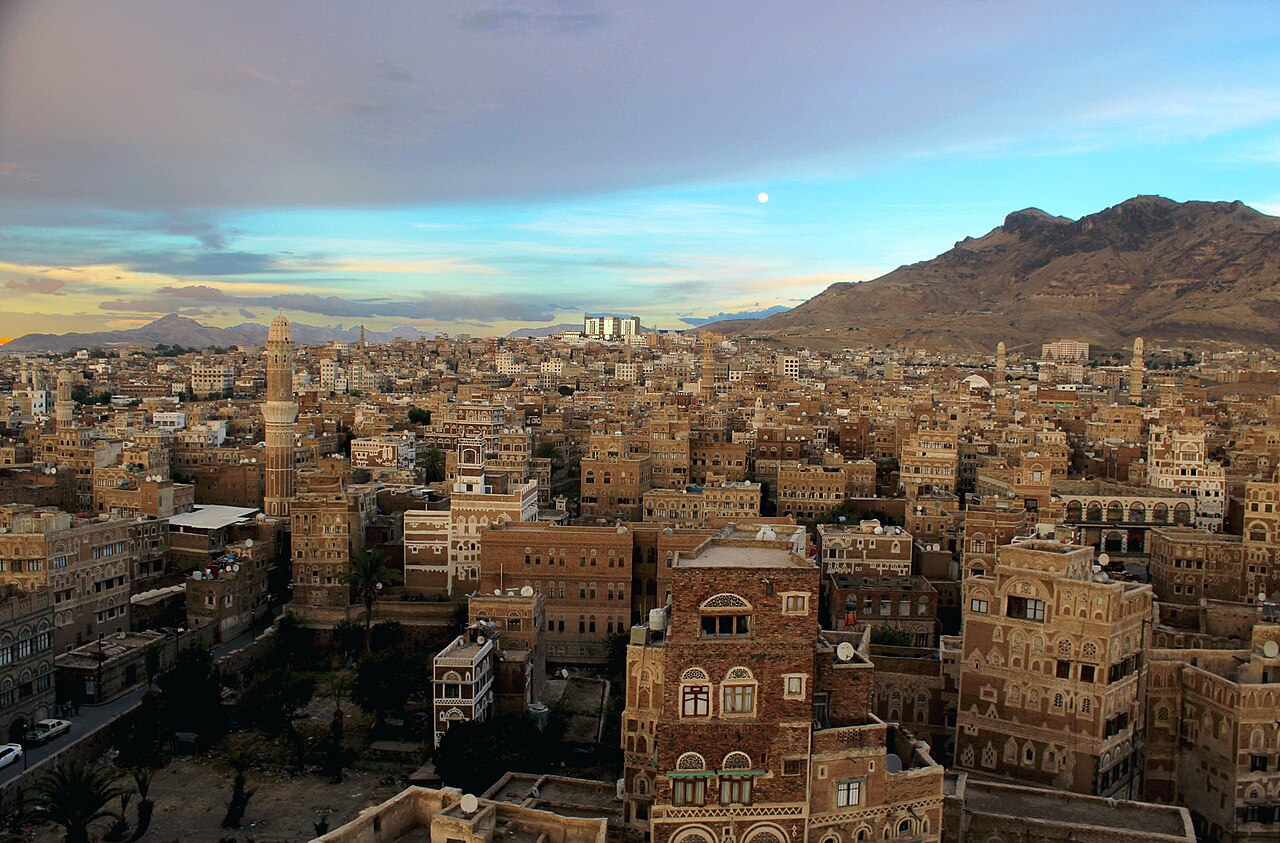 Old City of Sanaa's brick tower houses and a minaret at dusk, with mountains behind
