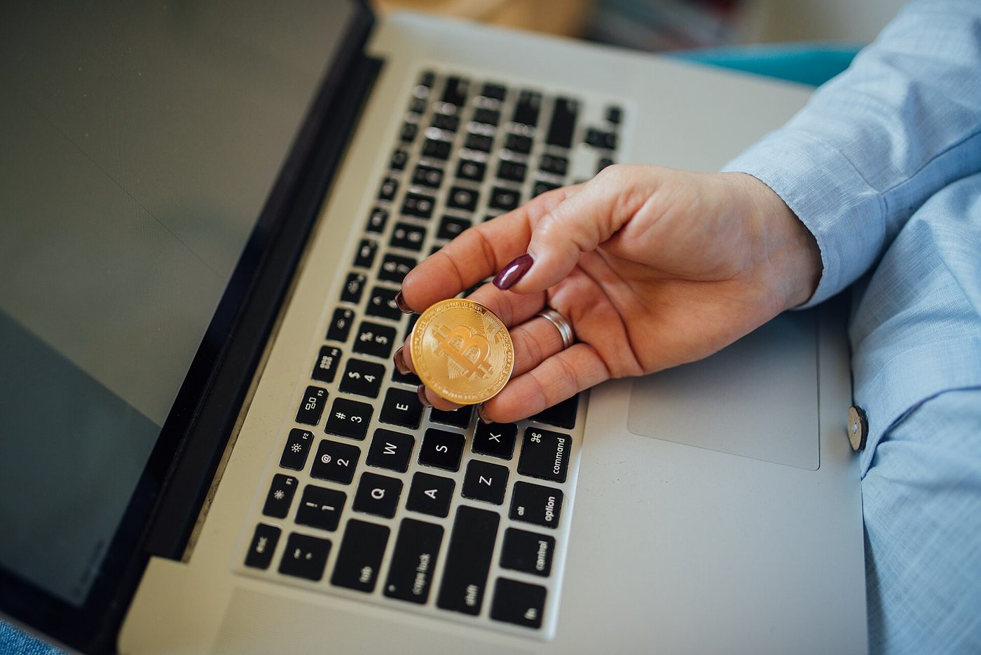 A physical bitcoin token held in a hand above a laptop