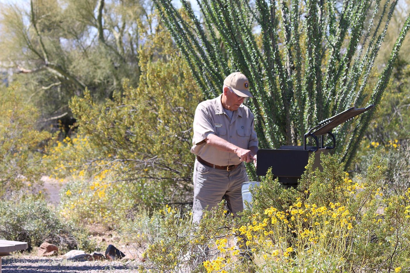 A volunteer cleans a campground grill with a brush