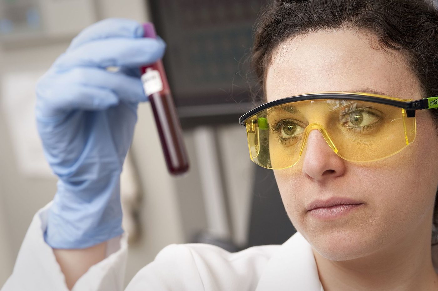 A National Eye Institute scientist in safety glasses checks a tube of blood