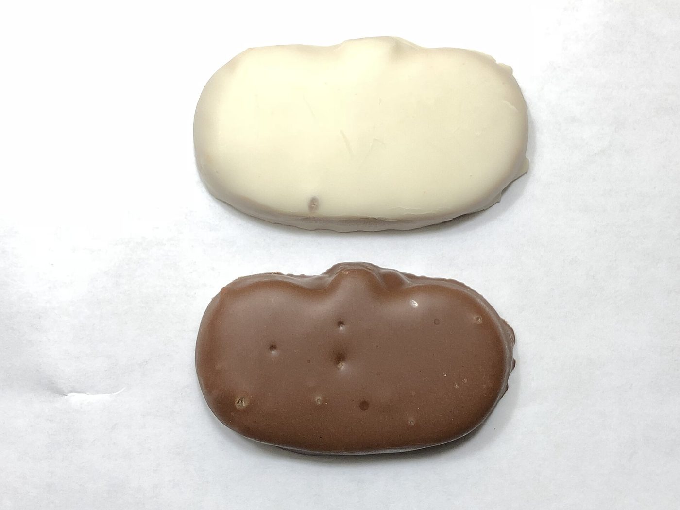 A Reese's Peanut Butter Pumpkin and a Reese's White Pumpkin, unwrapped, showing their plain uncarved surfaces