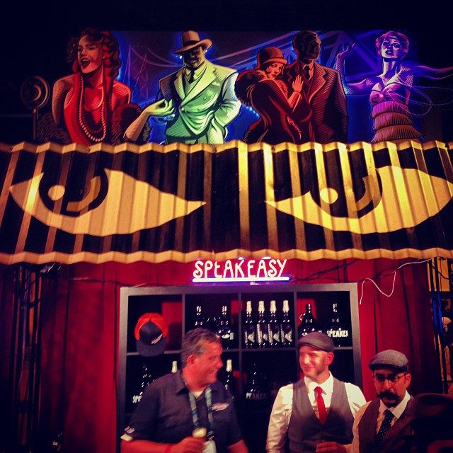 Brewers stand at the Speakeasy brewery booth, under a 1920s-style mural, at the 2013 Great American Beer Festival