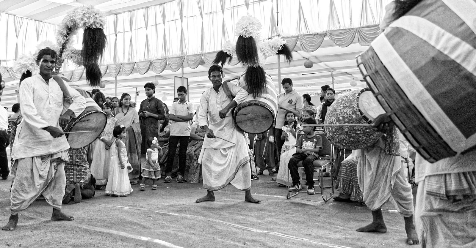 Black-and-white photo of dhakis playing large feather-topped dhak drums at a Durga Puja celebration in Delhi in 2015