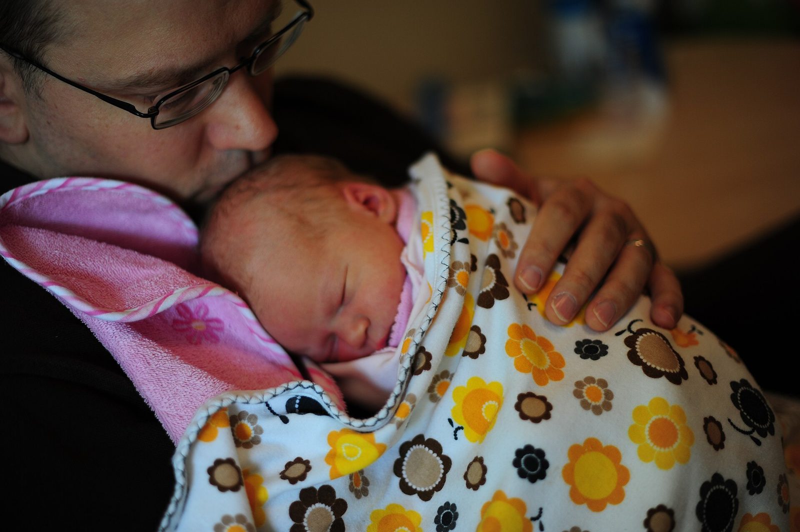 A human father cuddles his newborn-infant daughter, who has been wrapped in swaddling clothes