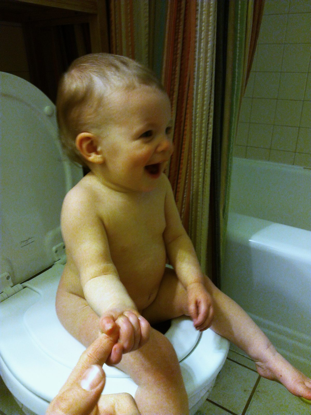 A toddler practicing sitting on the toilet (which is equipped with a child-size seat over the adult-size one)