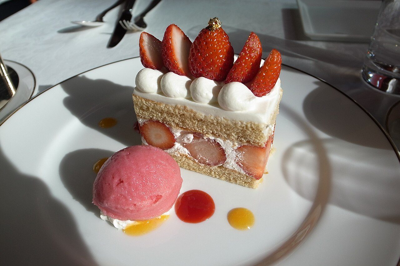 A slice of strawberry shortcake with cream and fresh strawberries