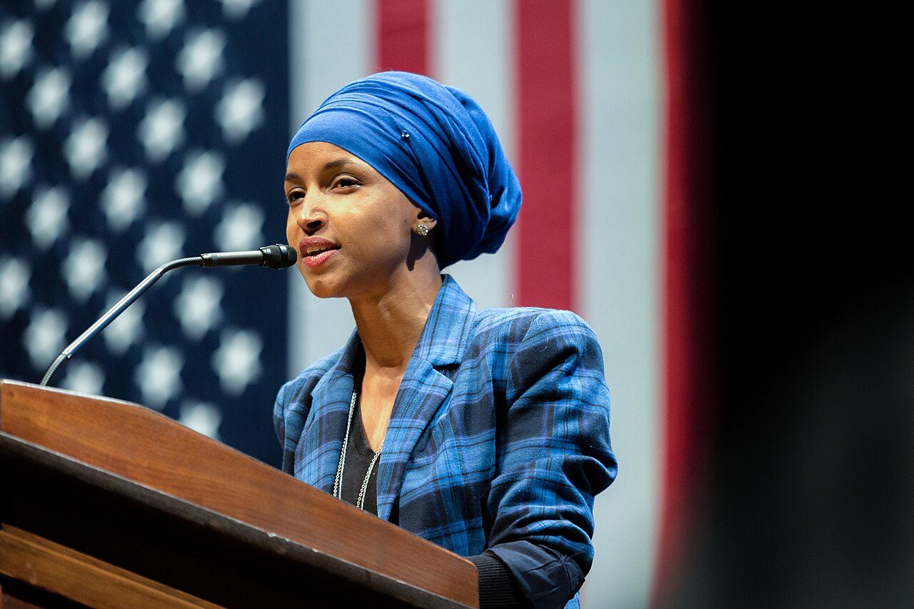Ilhan Omar speaking at a podium in front of an American flag