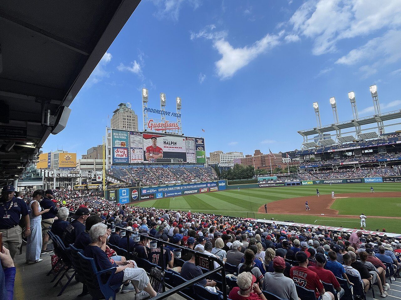 Fans fill the seats along the field at Progressive Field under a blue sky with scattered clouds
