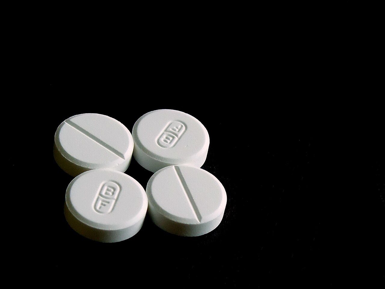 Four round white tablets on a black background