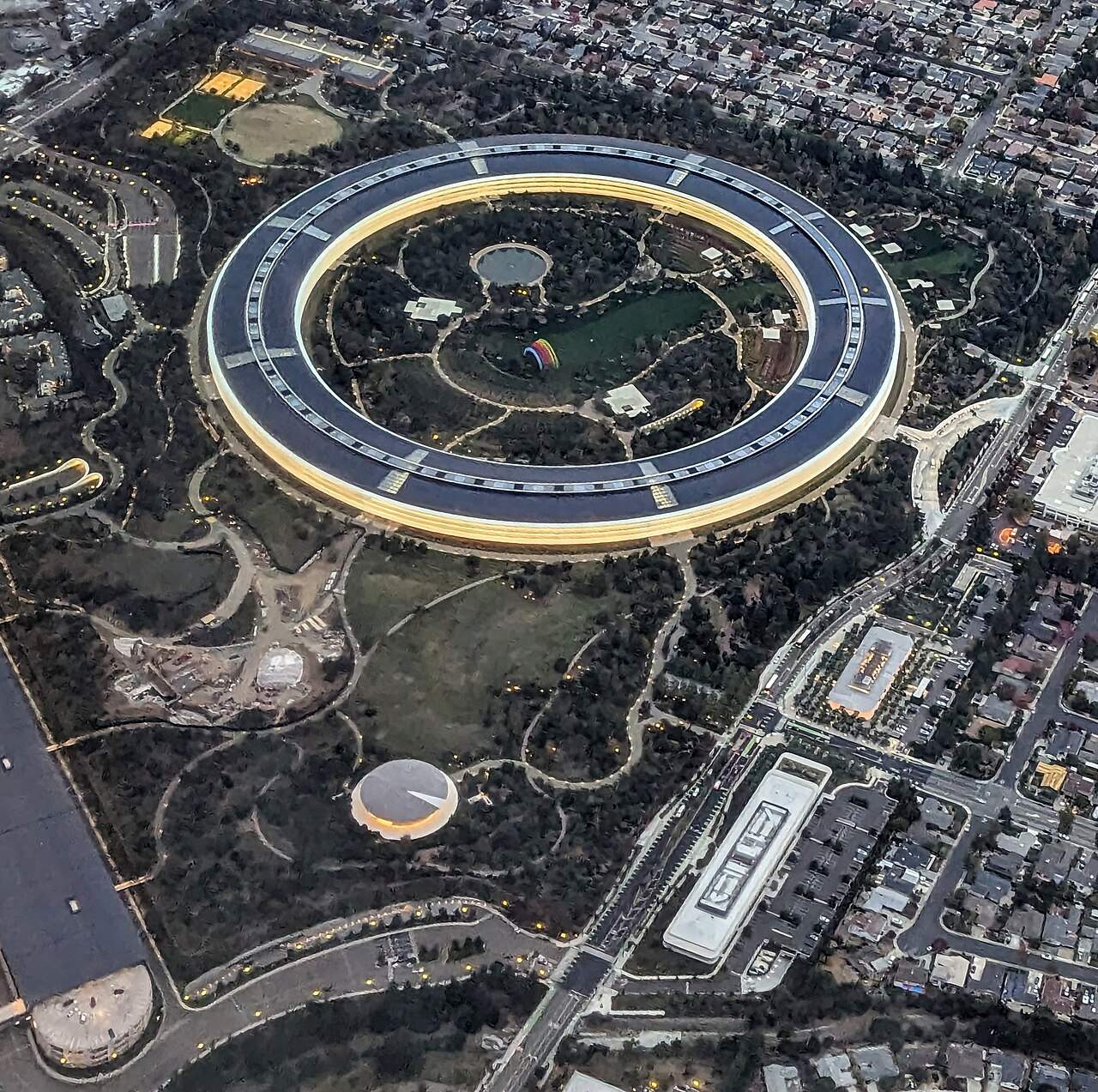 Aerial view of a huge ring-shaped building surrounded by trees and parking structures