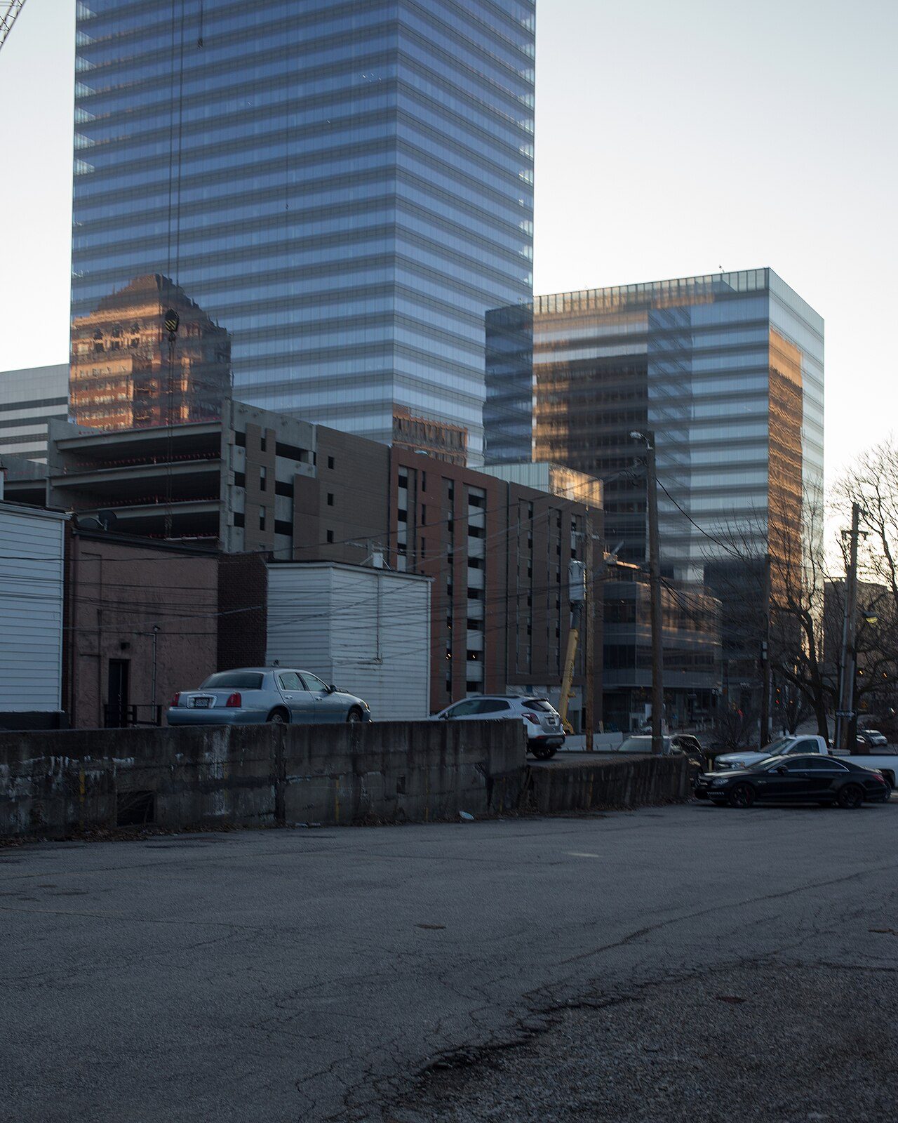 Tall glass office towers rise behind low buildings and a parking lot on a clear day