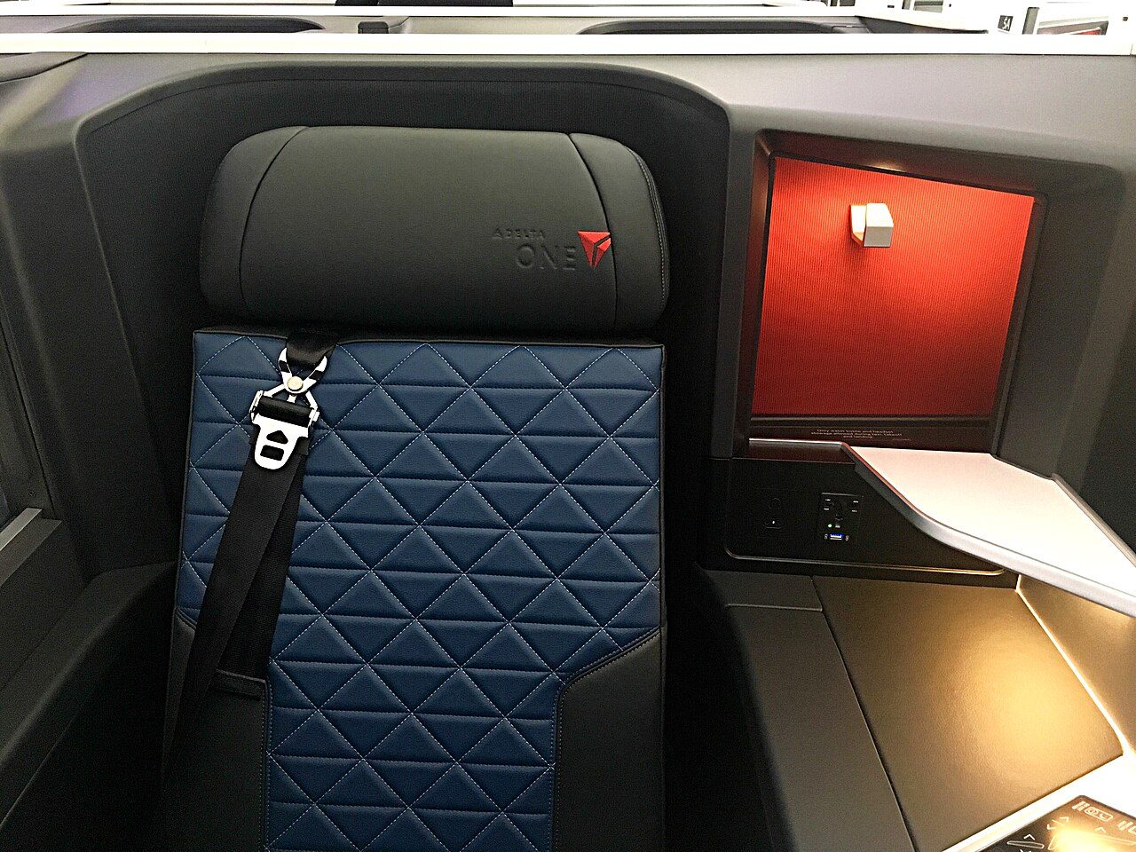 A Delta One business-class seat with dark blue quilted cushions and a red-lit panel