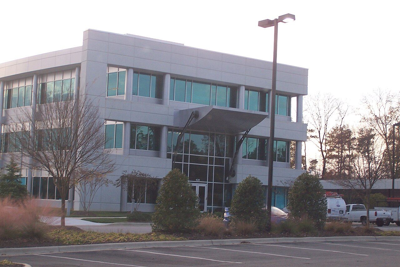 A modern gray office building with large windows and a parking lot in front