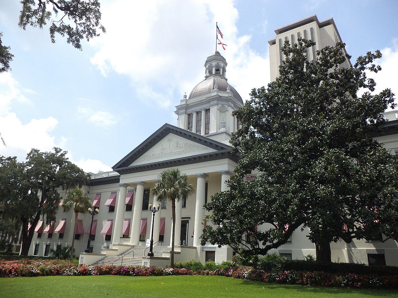 A white domed historic capitol building with red-and-white striped awnings in front of a tall modern tower
