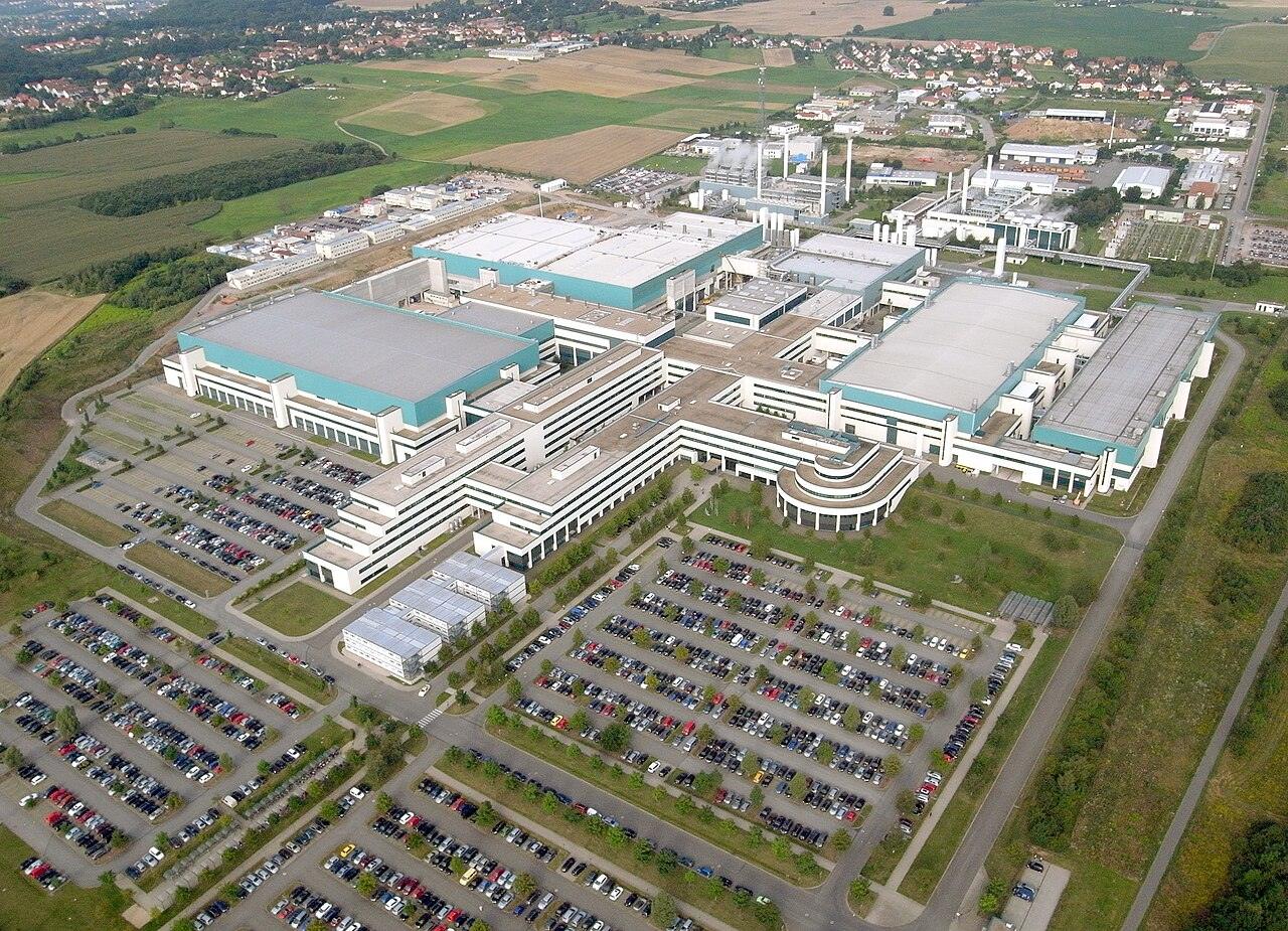 An aerial view of a large white semiconductor factory complex surrounded by fields