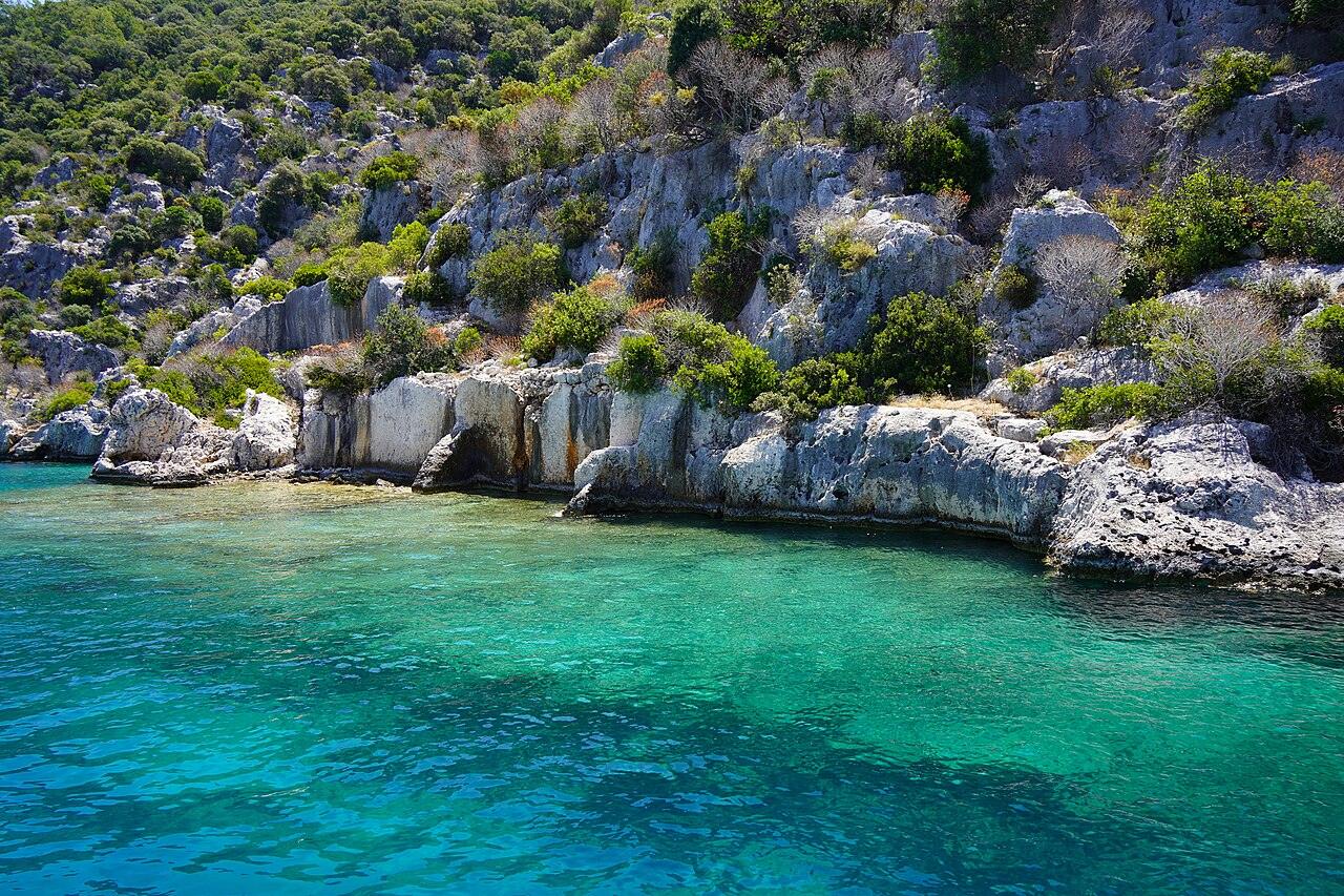 Ancient stone ruins on a rocky shore above clear turquoise water