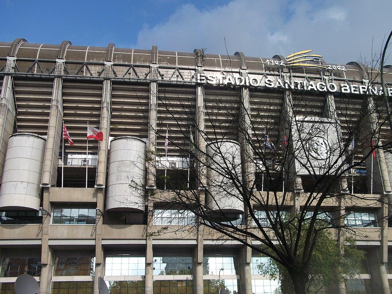 The large exterior of a football stadium with tall towers under a clear sky