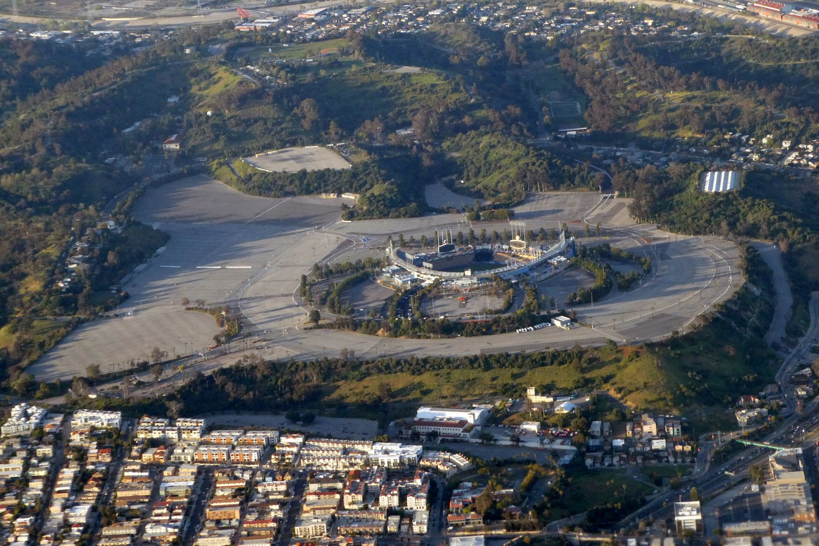 Aerial view of Dodger Stadium with empty parking lots, surrounded by green hills and nearby homes