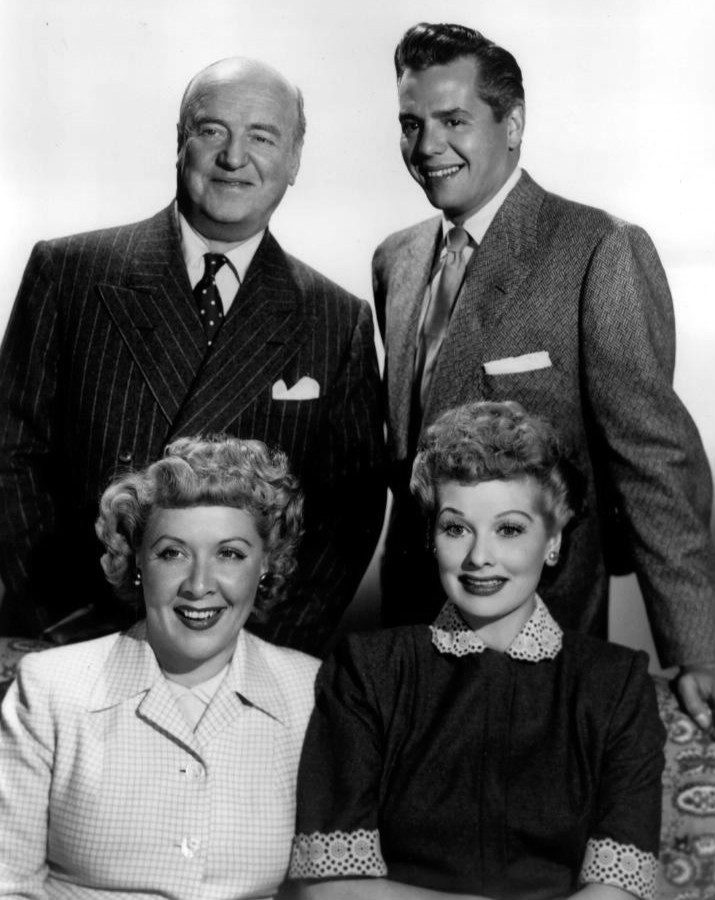 Black-and-white publicity photo of William Frawley and Desi Arnaz standing behind a seated Vivian Vance and Lucille Ball