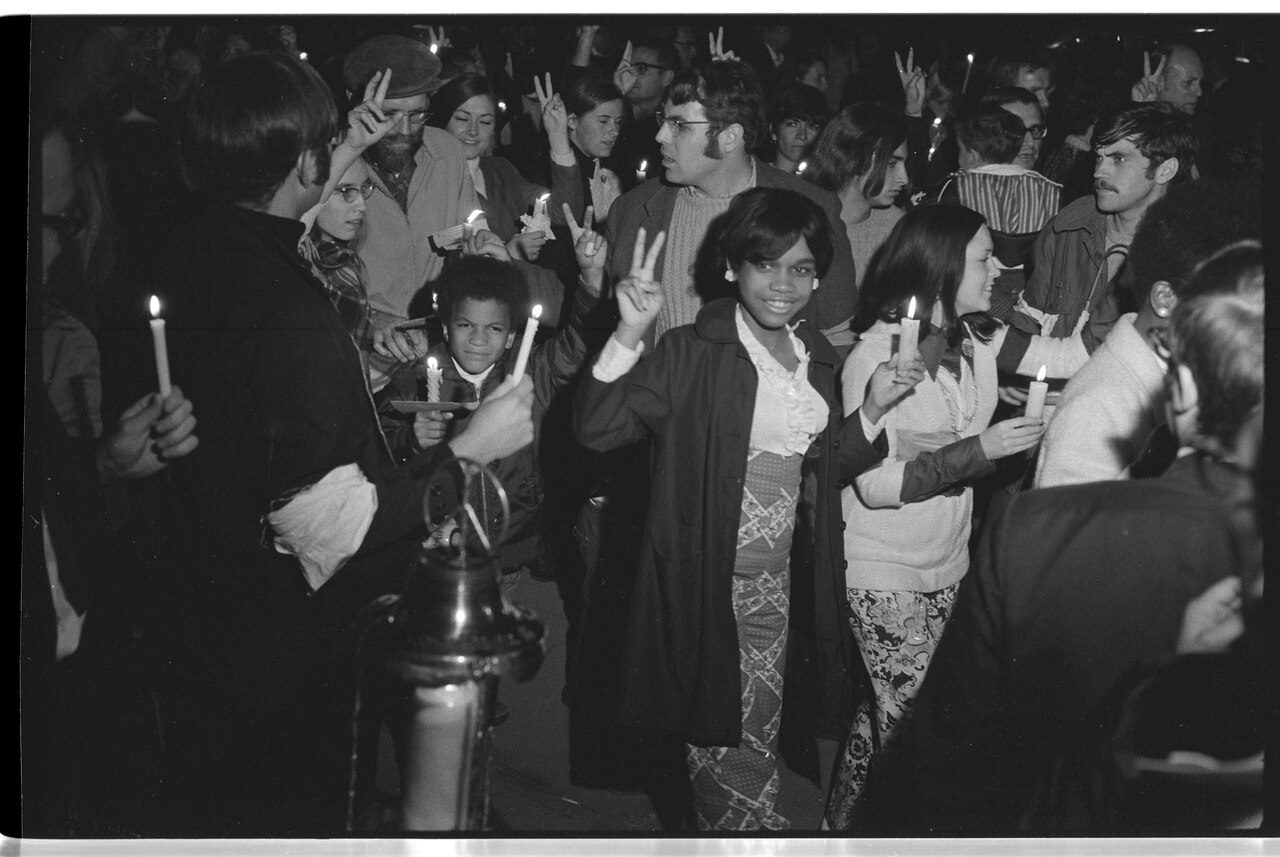 A black-and-white photo of a crowd holding candles at a nighttime vigil