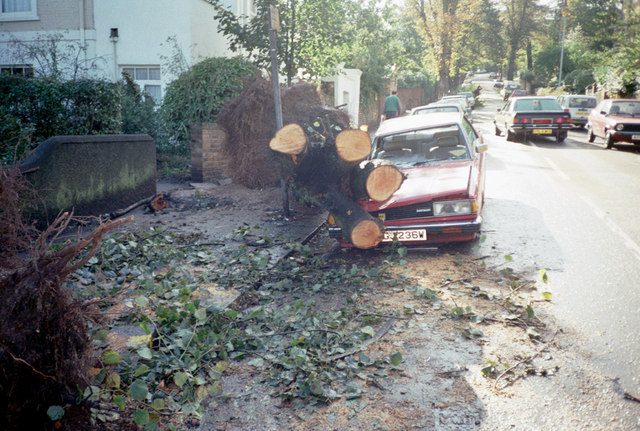 A sawn-up fallen tree trunk rests on a crushed red car beside a London street after the 1987 storm