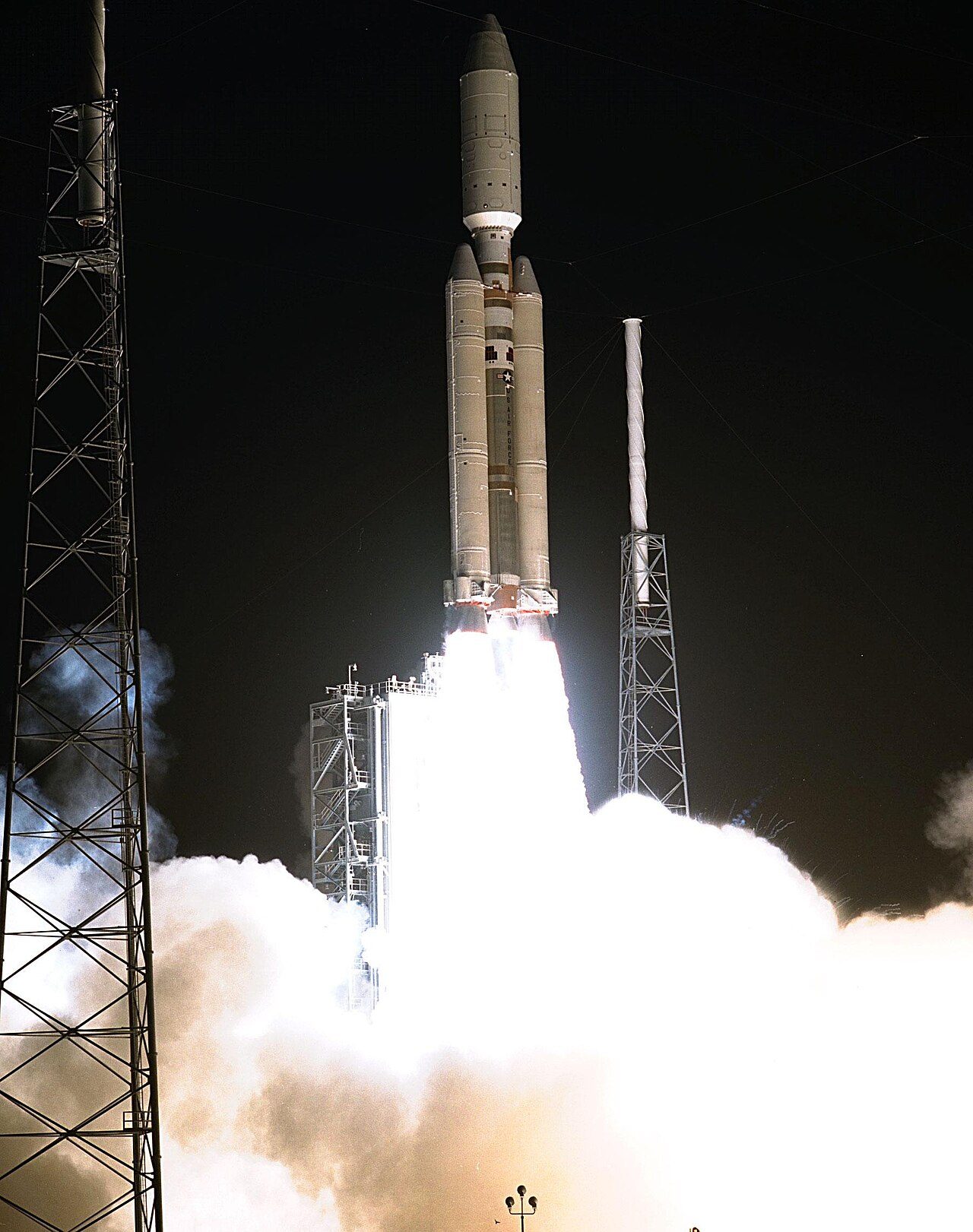 A Titan IVB rocket rises from its launch tower in the dark, with a bright plume of exhaust below