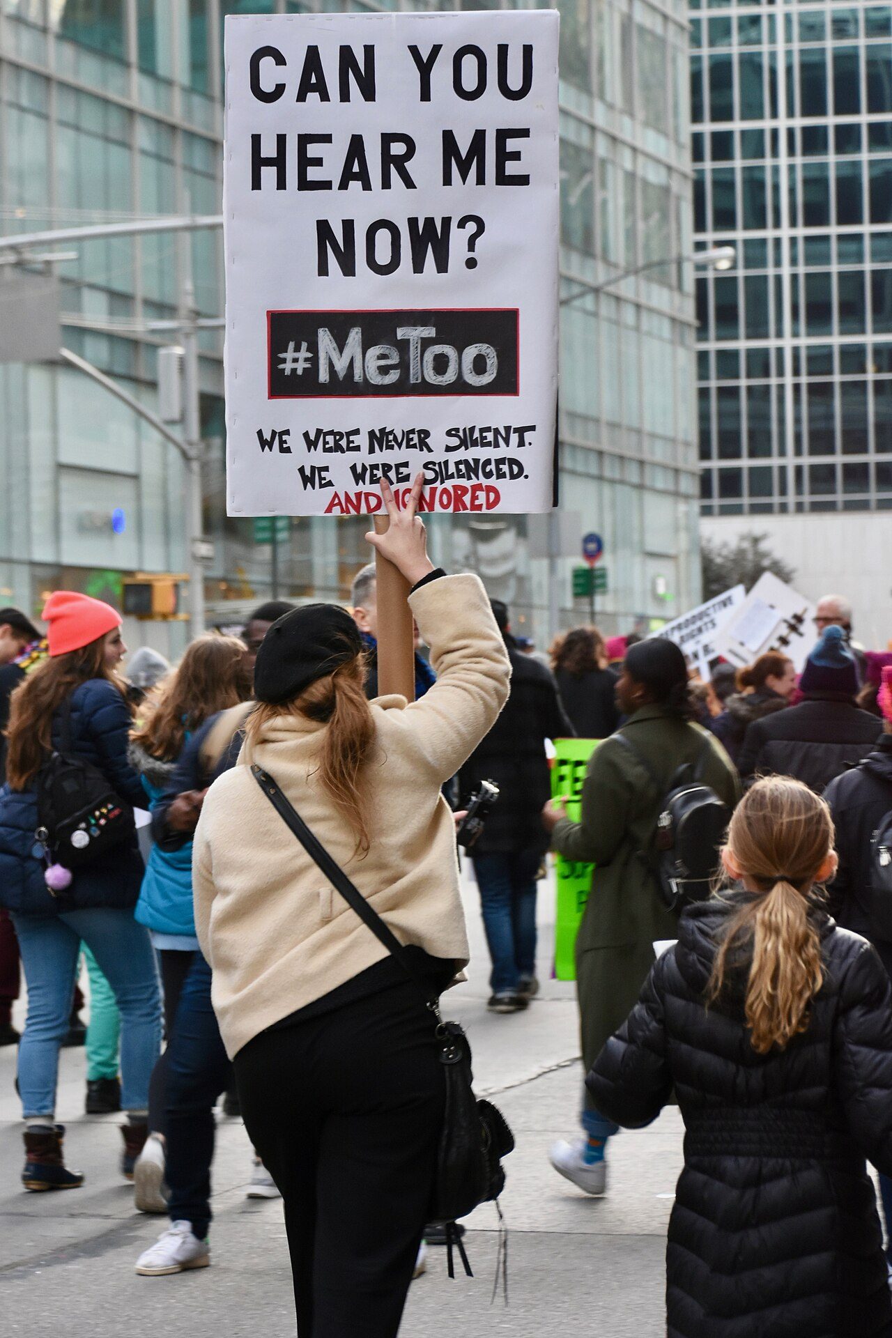 A woman holds up a sign reading Can You Hear Me Now? #MeToo at a street march