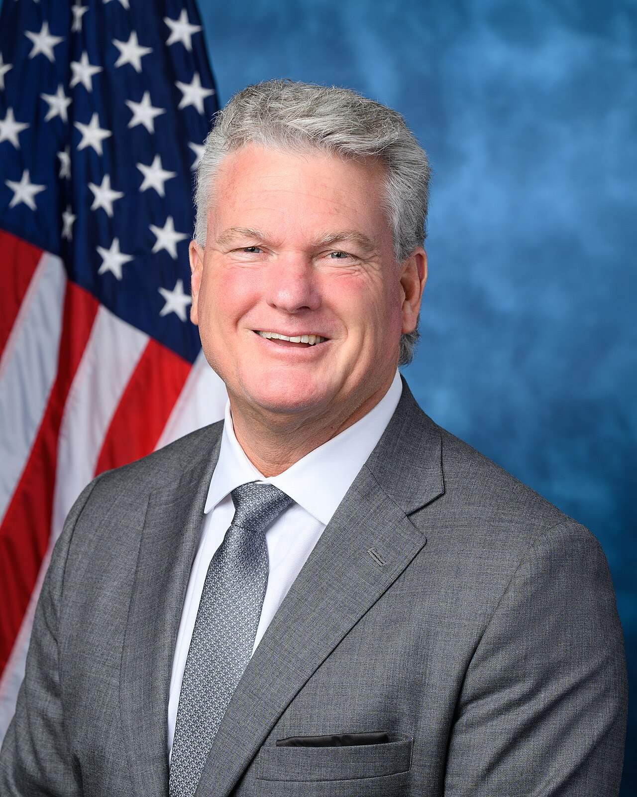 Official portrait of Rep. Mike Collins in a gray suit in front of an American flag