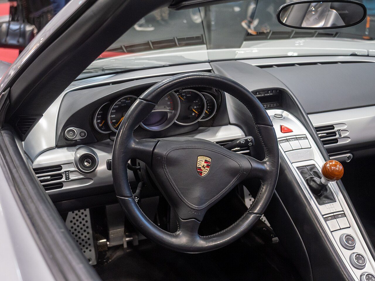 The cockpit of a silver Porsche Carrera GT, with the Porsche crest on the steering wheel and a wooden gear knob