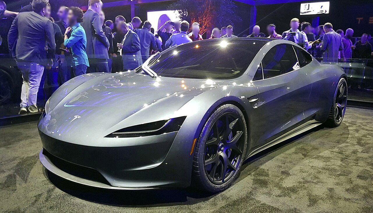 A silver low-slung sports car on display in front of a crowd of people
