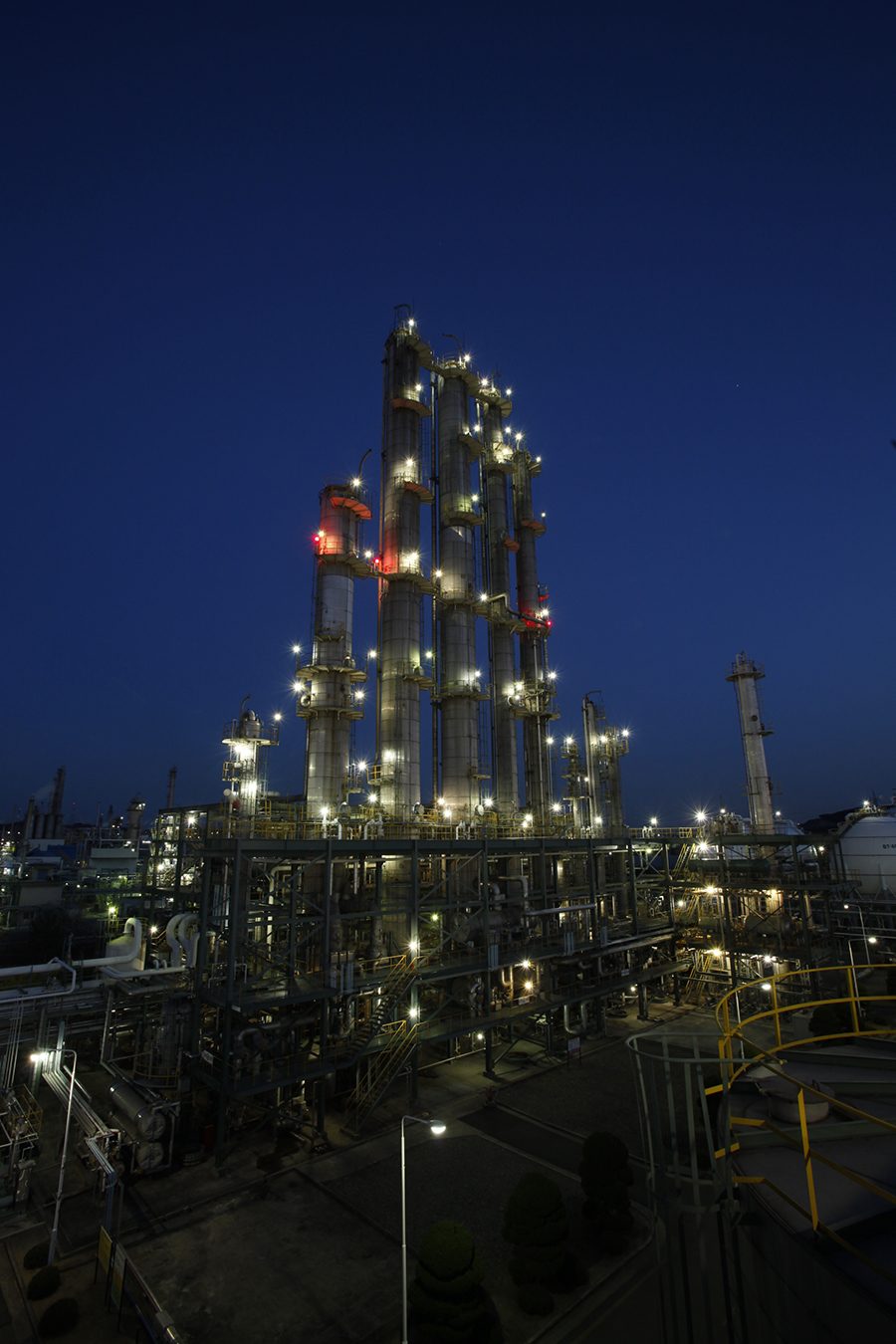 A chemical plant's towers and pipes lit up at night against a dark blue sky