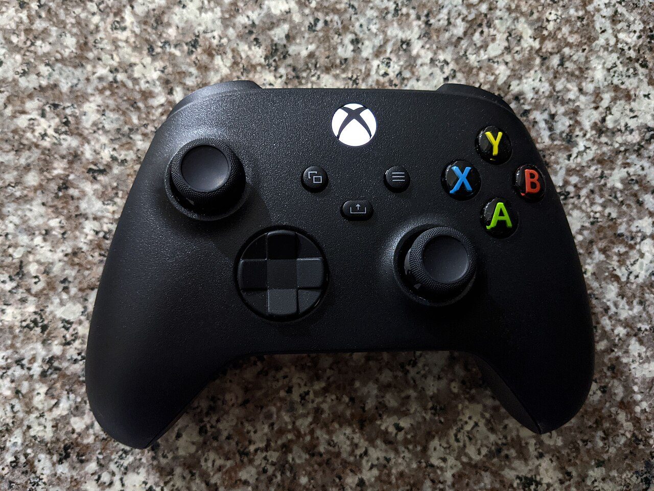 A black Xbox game controller lying on a speckled granite countertop