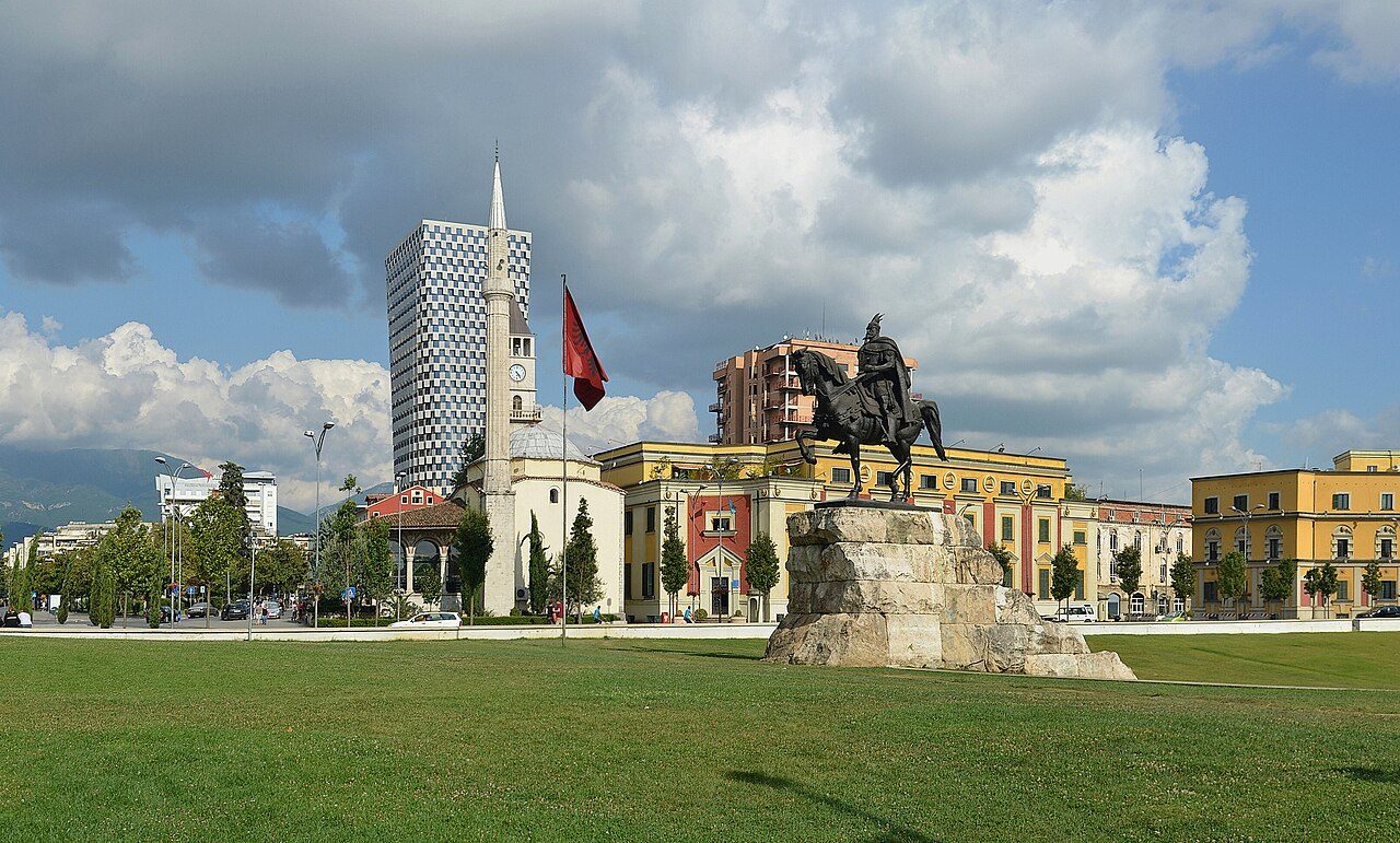 A wide public square with a statue of a man on horseback, trees and tall buildings under a cloudy sky