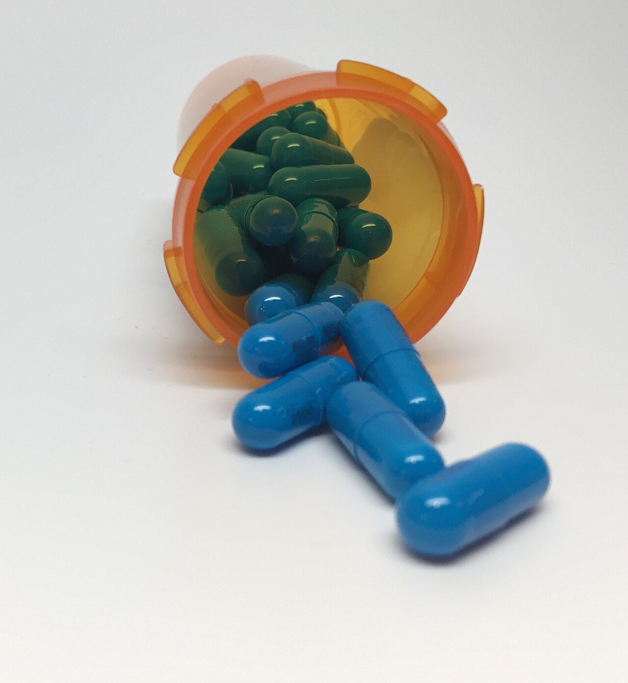Blue capsules spilling out of an orange prescription bottle on a white surface