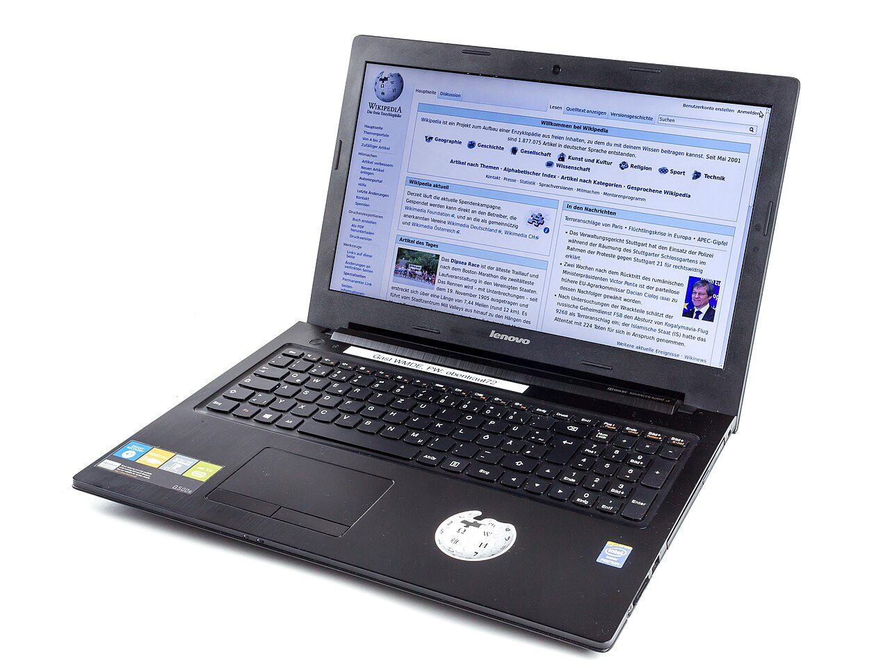 An open black Lenovo laptop on a white background, its screen showing a Wikipedia main page in German