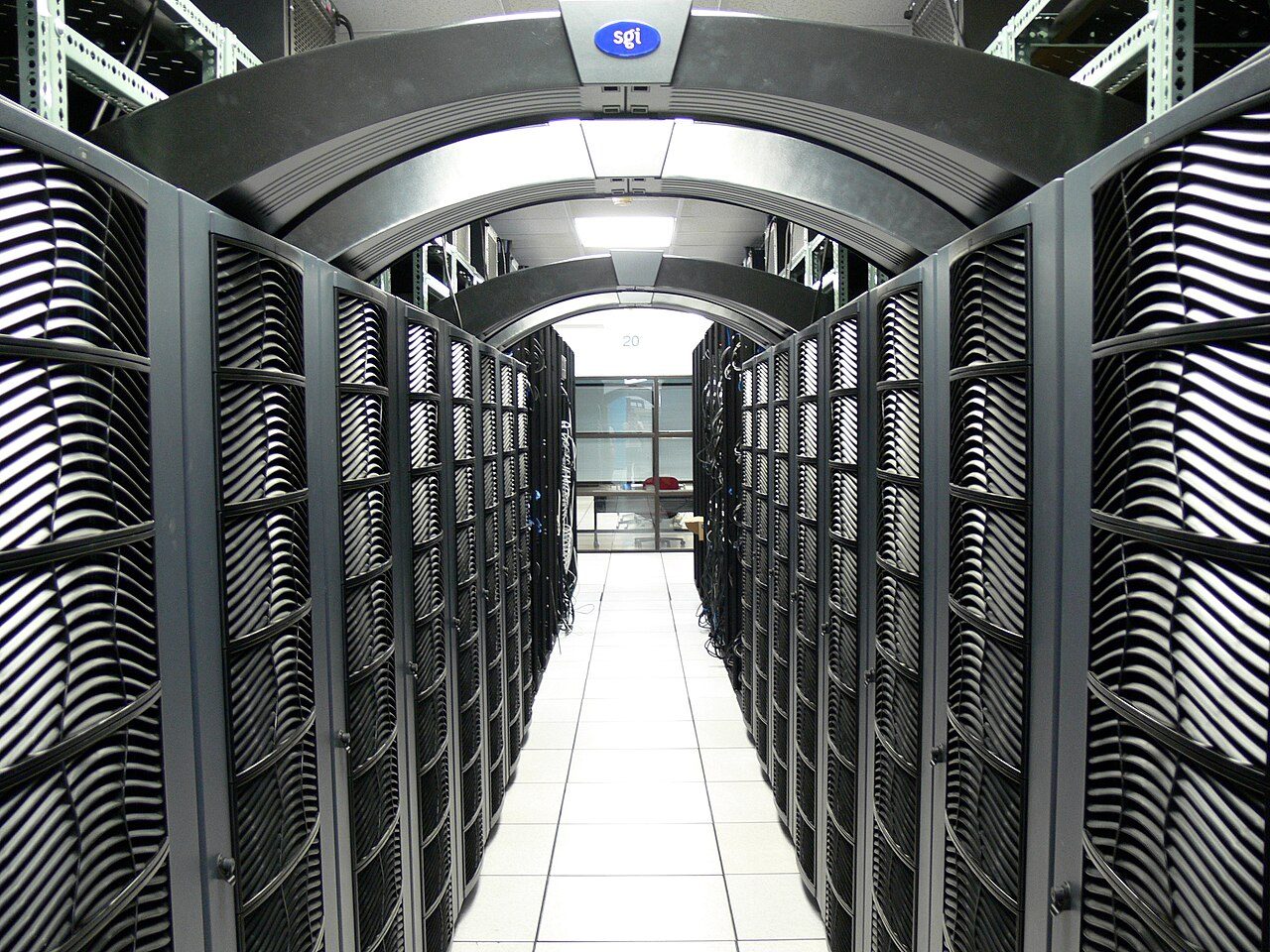 A long, narrow aisle between rows of tall black server cabinets with curved fronts, under bright ceiling lights