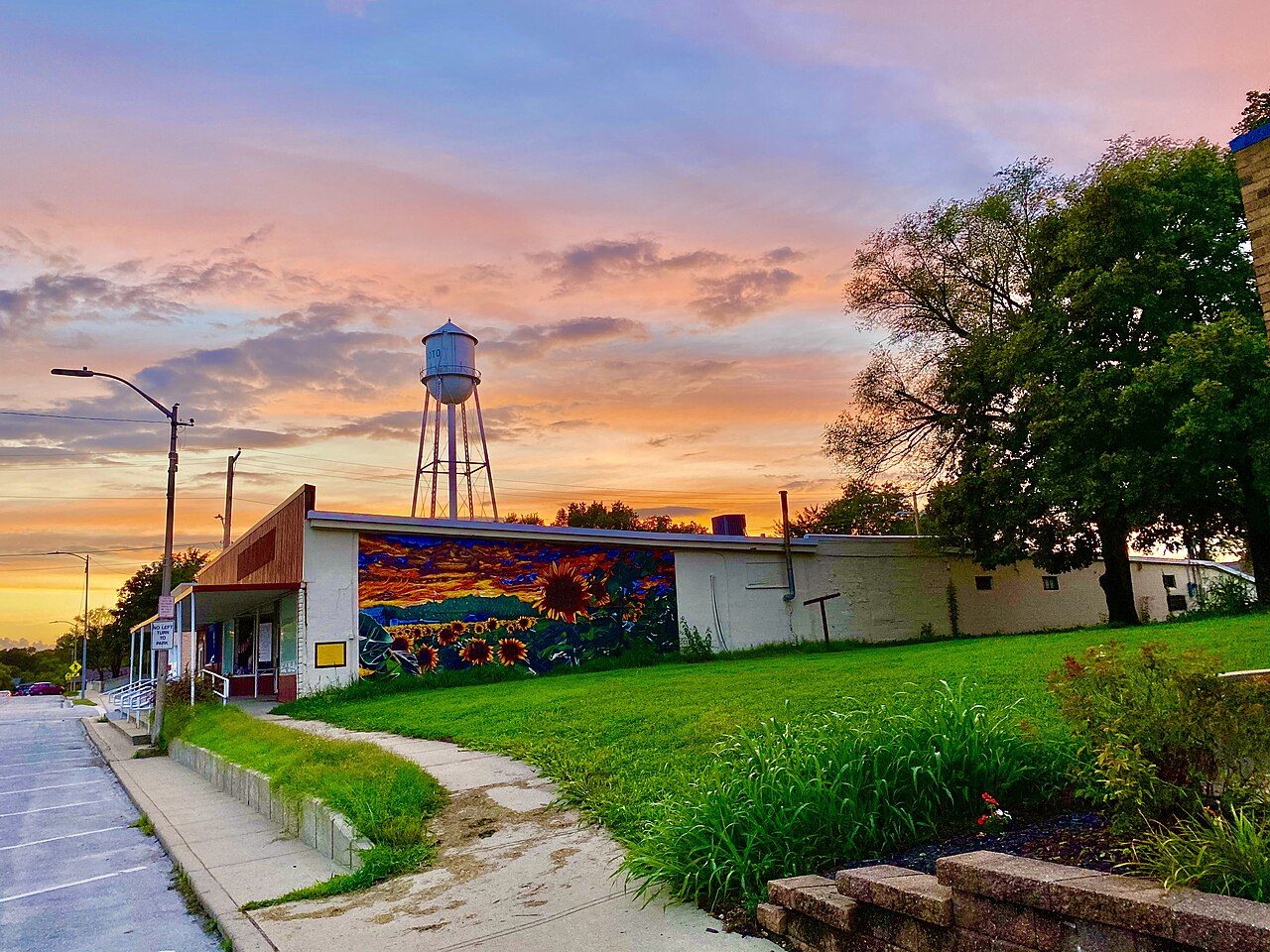 A water tower and a colorful mural on a low building under a pink and orange sunset sky