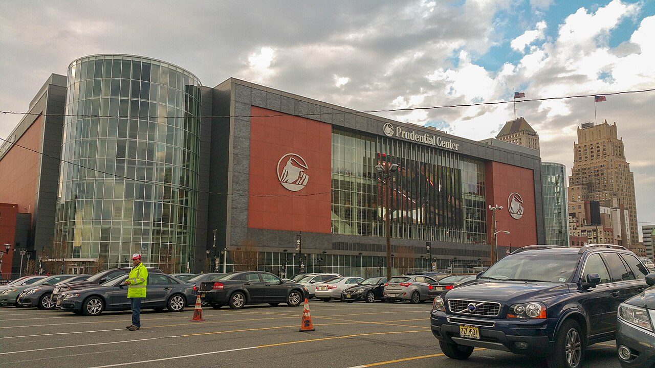 The glass and red brick front of a large arena with cars in the parking lot in front