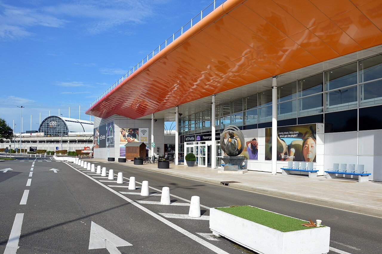 A low terminal building with an orange roof beside an empty road with white bollards
