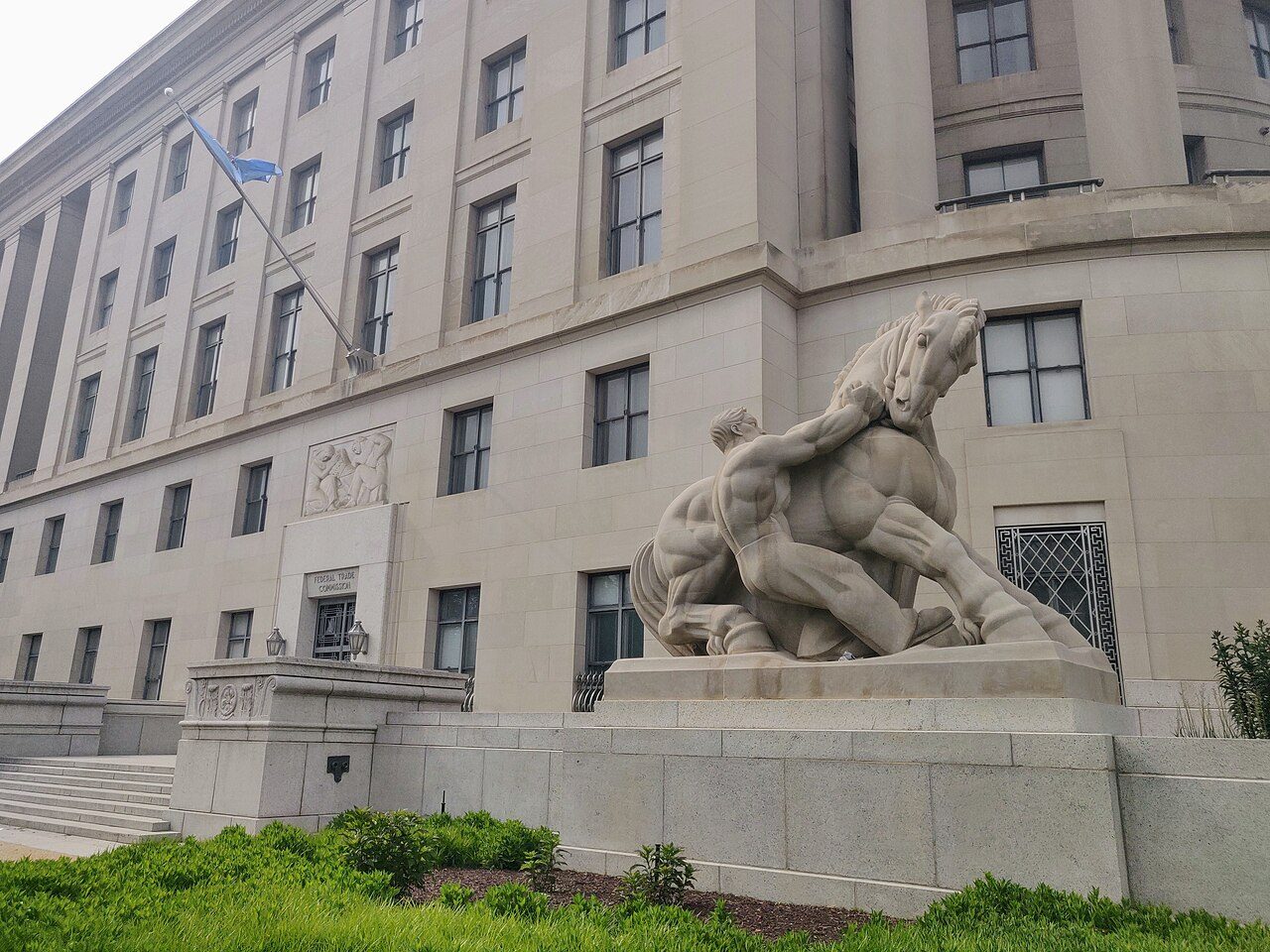 A large stone government building with a sculpture of a man restraining a horse in front