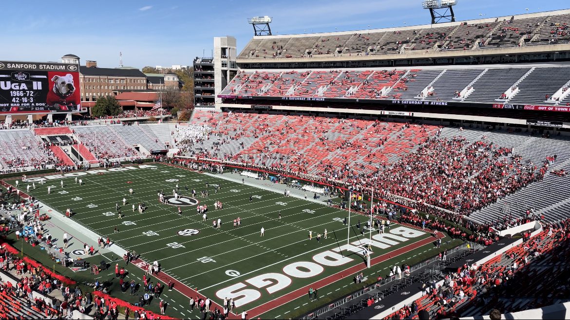 A college football stadium with red seats filled with fans and a green field marked with the word Dawgs in the end zone