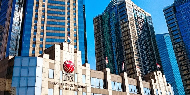A low building with an IDX Indonesia Stock Exchange sign and red logo sits in front of tall blue glass office towers under a clear sky