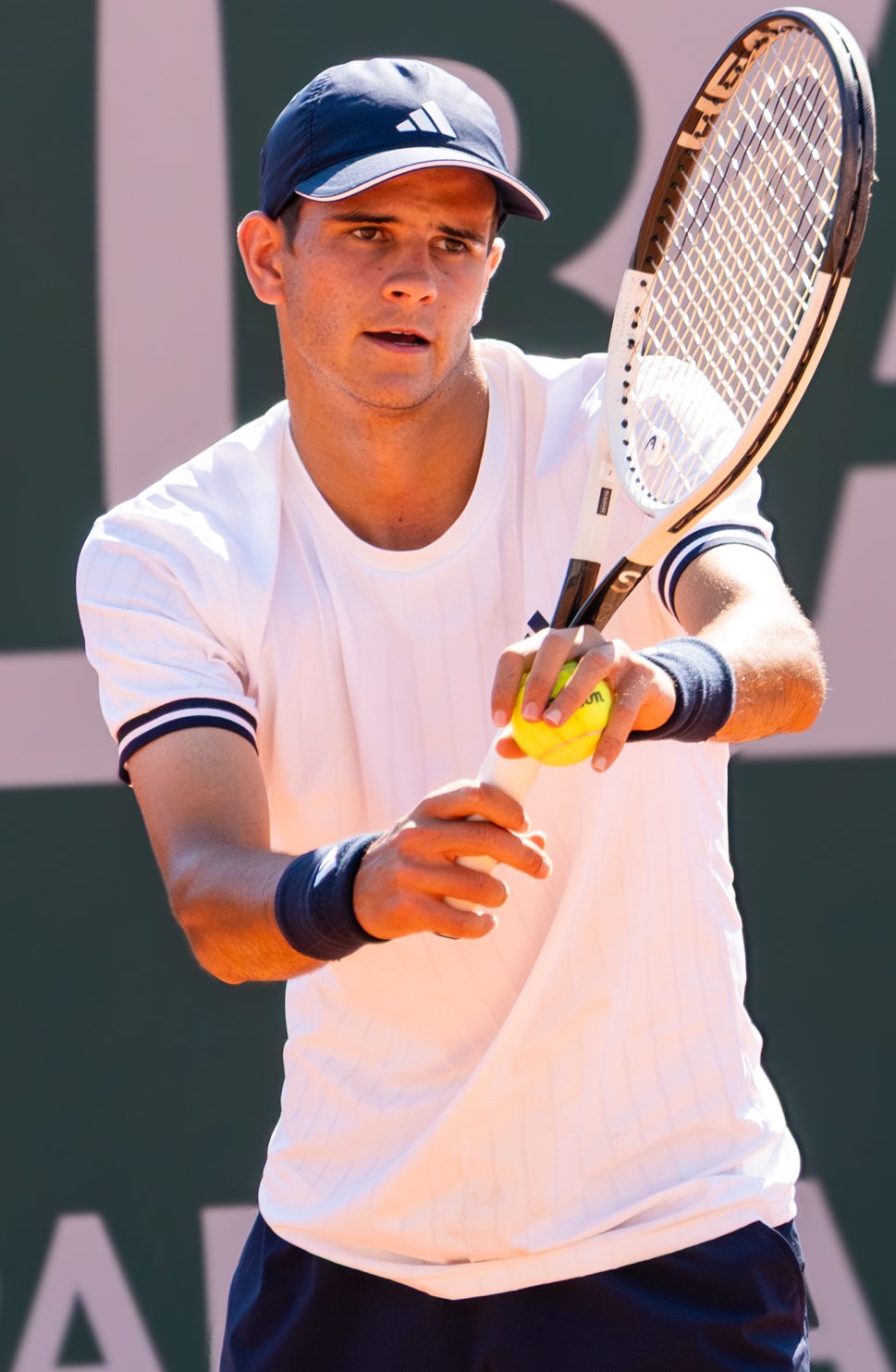 Rafael Jódar in a white shirt and cap holding a tennis racket as he gets ready to serve