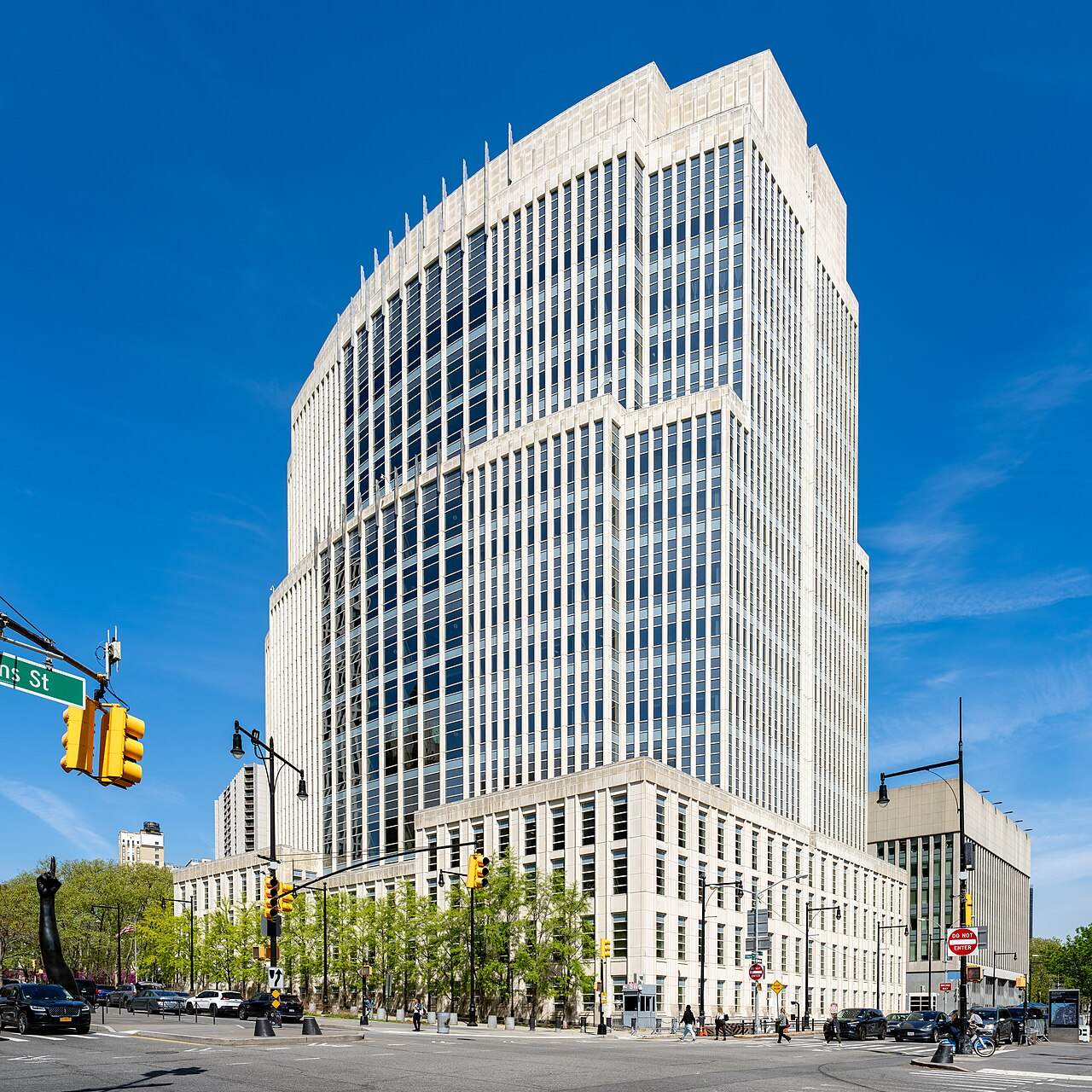 A tall modern courthouse tower with a glass facade next to a city street under a blue sky