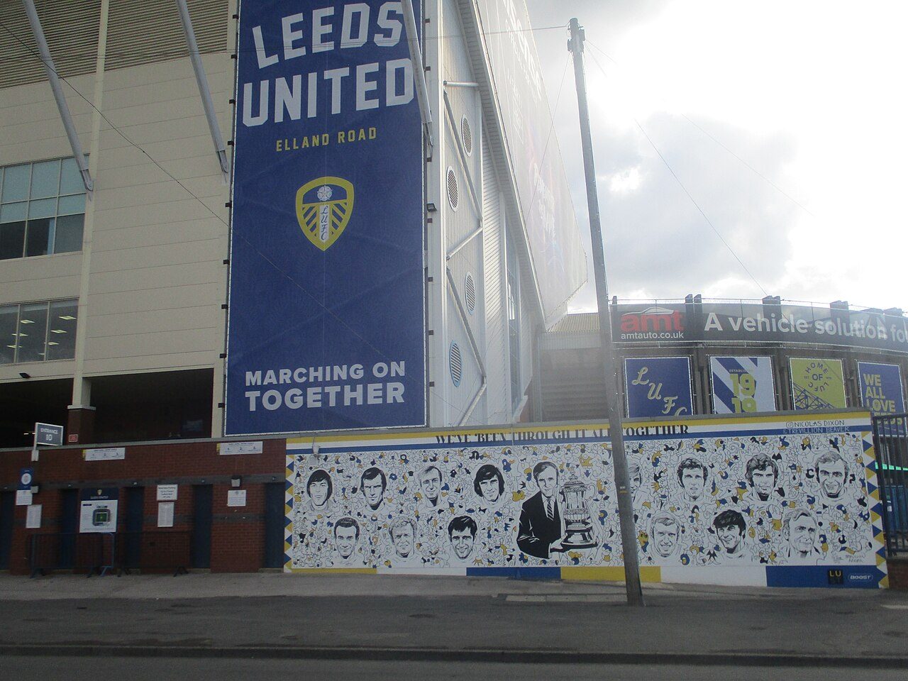 The outside of a soccer stadium with a large Leeds United banner and a mural along the wall
